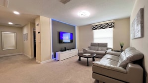 A living room with a flat-screen TV, a beige sofa, a coffee table, and a wall-mounted TV.