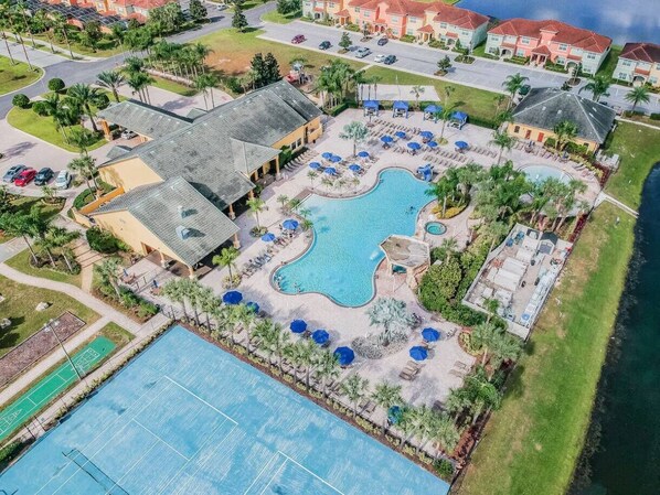 An aerial view of a resort with a large swimming pool, tennis courts, and a beachfront.