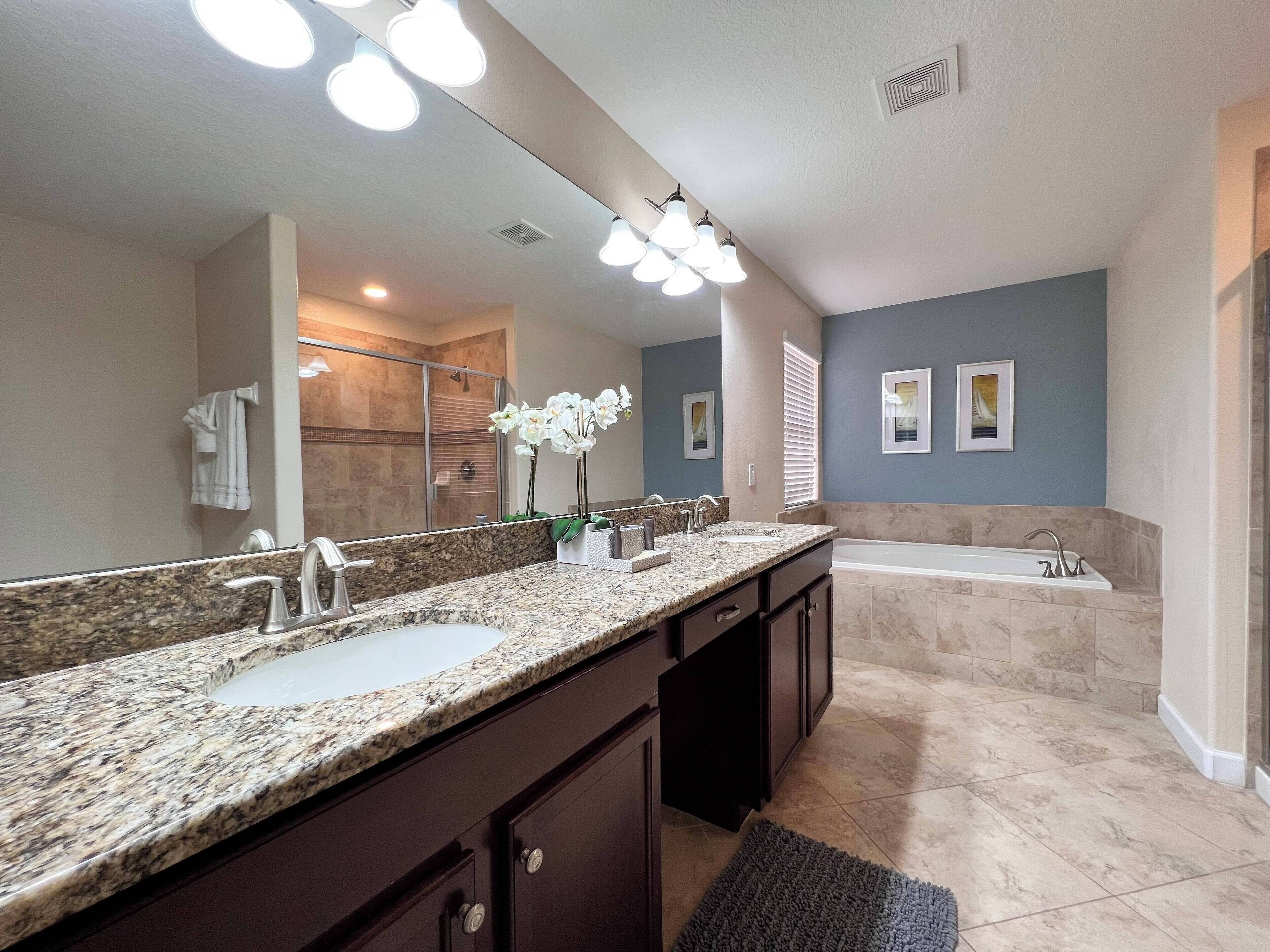 A modern bathroom with a granite countertop, a large mirror, a shower, and a bathtub.