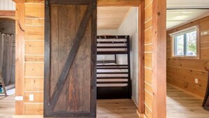 Un interior de madera con una puerta corrediza que da a una zona superior con una cama litera.