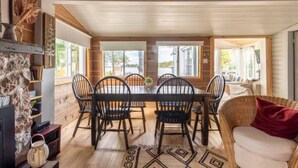 Un comedor con una mesa y sillas de madera, chimenea y ventanas amplias.