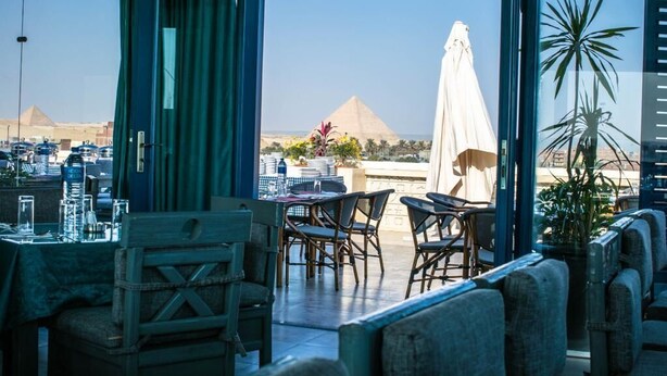Une terrasse ouverte offrant une vue sur les pyramides, des sièges en plein air et une table dressée pour le dîner.