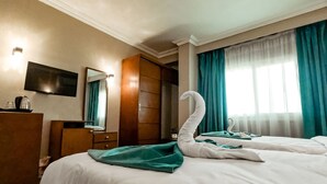 Une chambre d’hôtel avec deux lits, une armoire en bois, un téléviseur à écran plat et une grande fenêtre avec des rideaux.