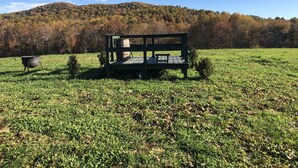 Una panxa de fusta amb un barril metàl·lic en un camp herbós, amb un turó forestal al fons.