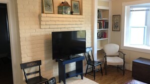 Un saló amb una llar de pedra, un televisor de pantalla plana, una biblioteca i una finestra.
