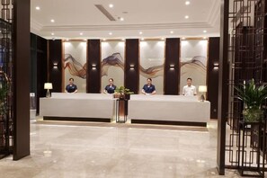 A reception area with a reception desk, three staff members, and a potted plant. - BBH Hotel (Xinchang Ocean City) (Xinchang)