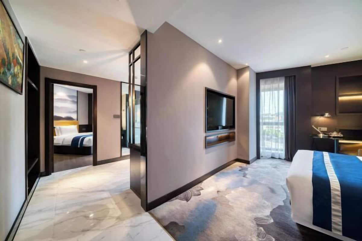 A modern hotel room with a large bed, a flat-screen TV, a desk with a chair, and a view of the city through the window.