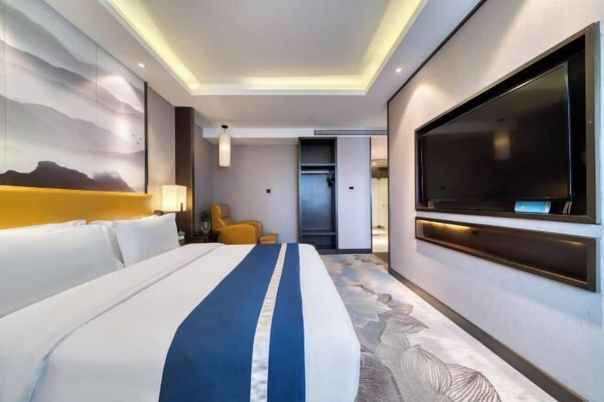 A modern hotel room with a large bed, a flat-screen TV, and a view of the mountains.