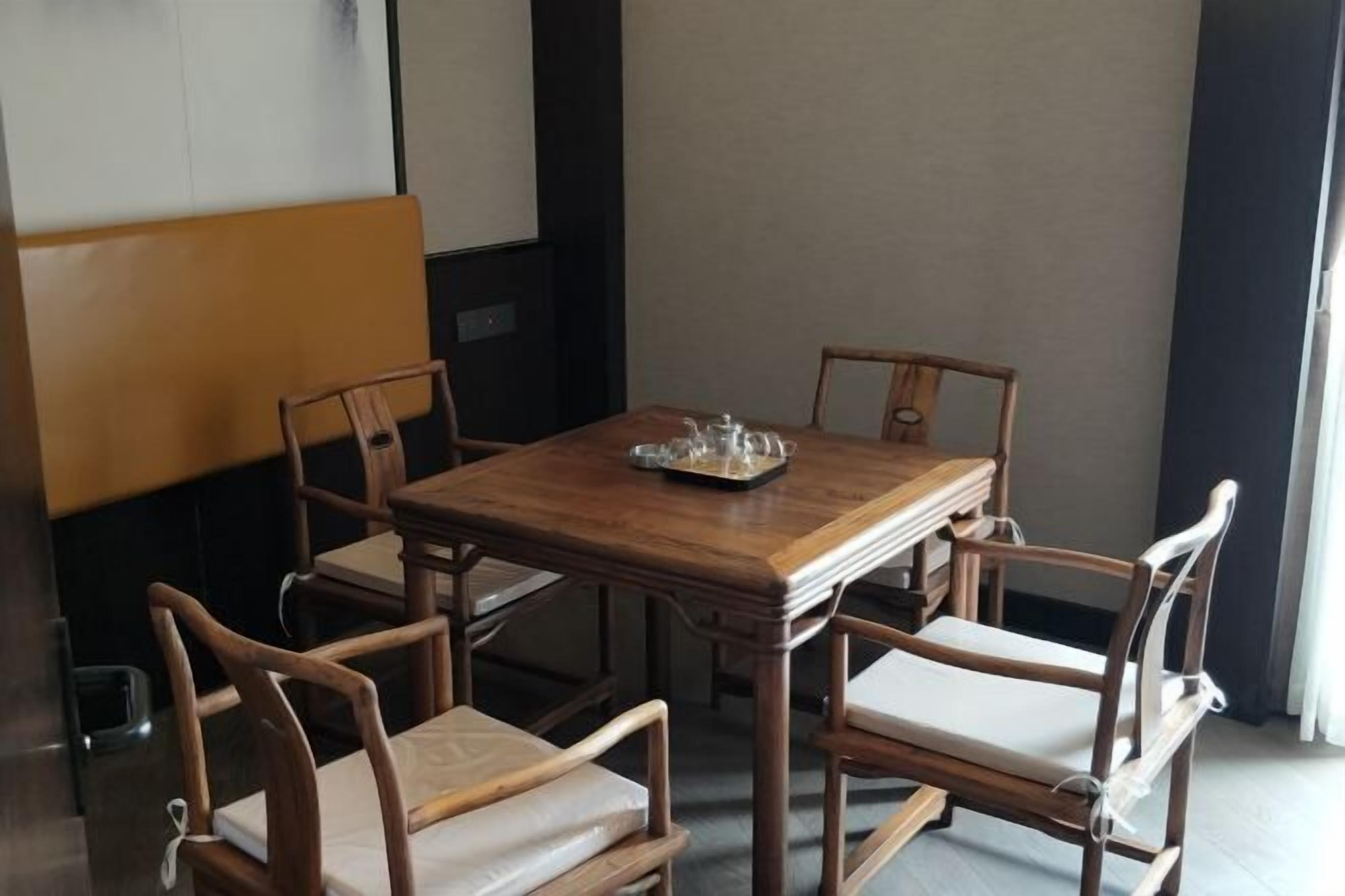 Un comedor con una mesa de madera y cuatro sillas, una bandeja con cristalería y vista a un edificio.