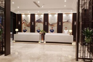 Zona de recepción con diseño moderno, que incluye un mostrador de recepción, tres empleados y una pared decorativa con arte abstracto.