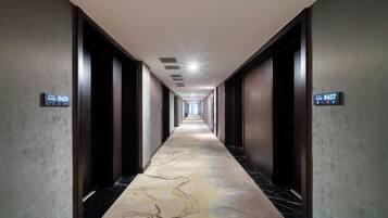 A long, narrow hallway with a patterned carpet, doors on either side, and a digital clock displaying the time.
