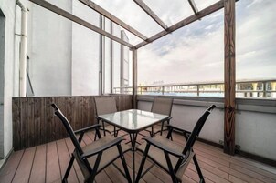 Un espacio de estar al aire libre con techo, con una mesa y sillas, que da vista a un puente y al agua.
