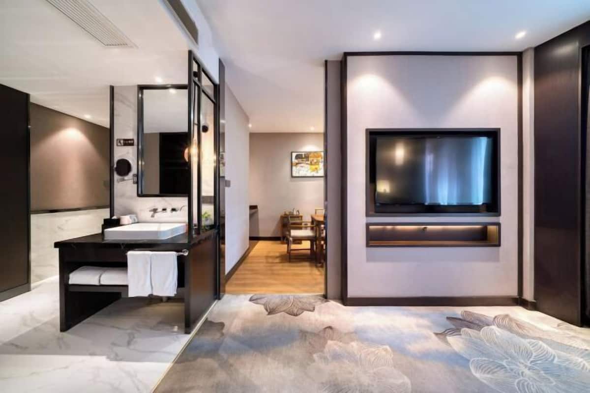 A modern bathroom with a large mirror, a vanity with a sink, and a flat-screen TV mounted on the wall.