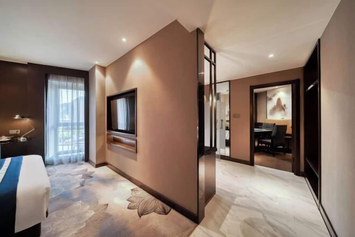 A modern hotel room with a bed, a TV, a desk, and a dining area.