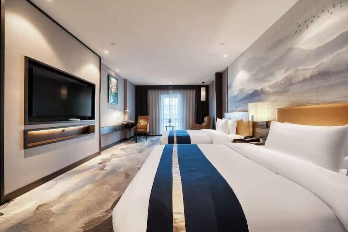 A hotel room with a large bed, a flat-screen TV, a desk, and a painting on the wall.