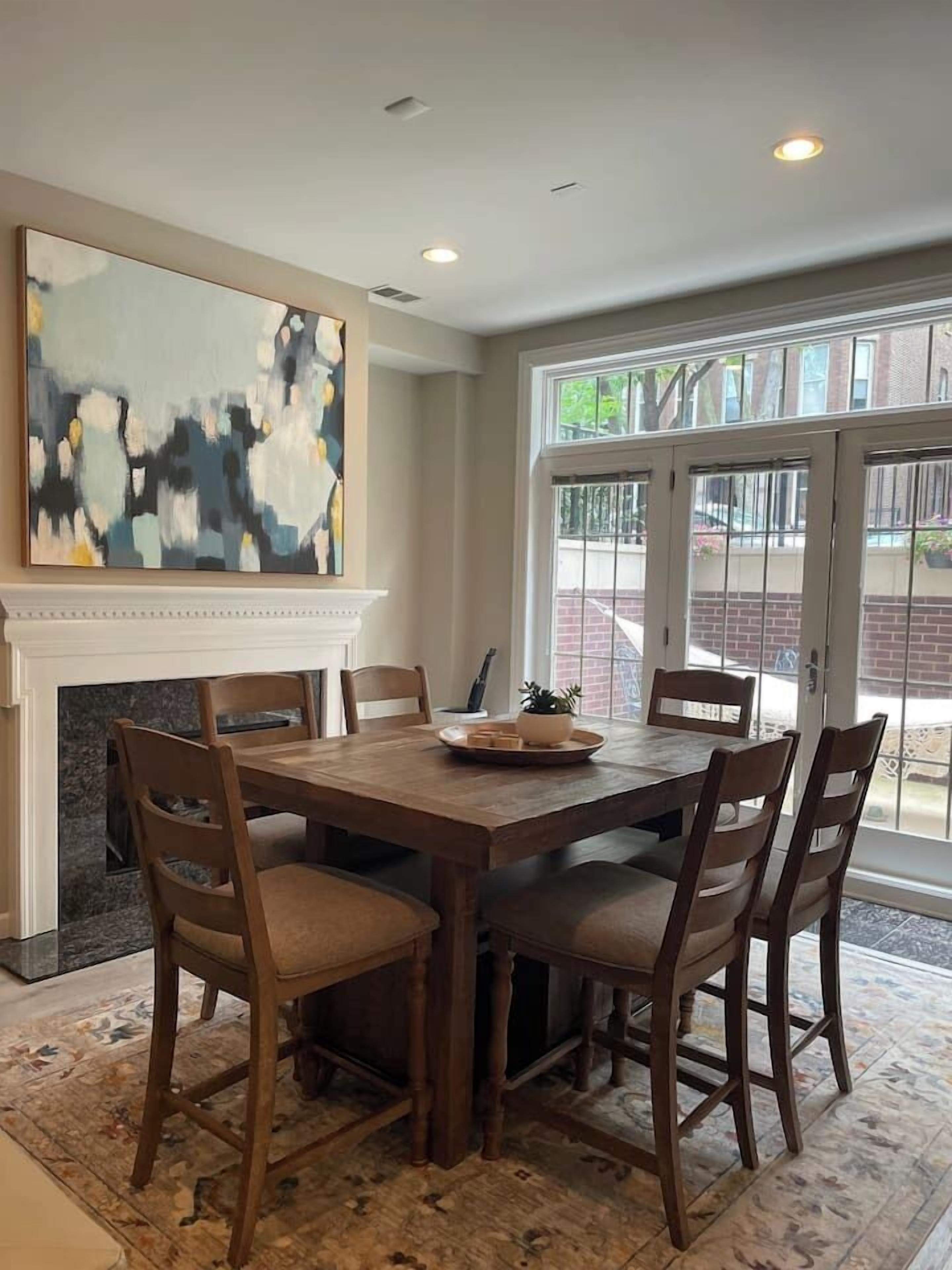 A dining area with a wooden table and chairs, a fireplace, and a large abstract painting on the wall.