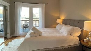 A bedroom with a bed, a ceiling fan, a nightstand, a lamp, and a view of the outside through a window. - Ukrainian Village 3BR/3BA • Private Patio, Parking (Chicago)