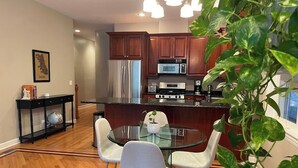 A modern kitchen with wooden cabinets, stainless steel appliances, and a glass dining table with chairs. - Ukrainian Village 3BR/3BA • Private Patio, Parking (Chicago)
