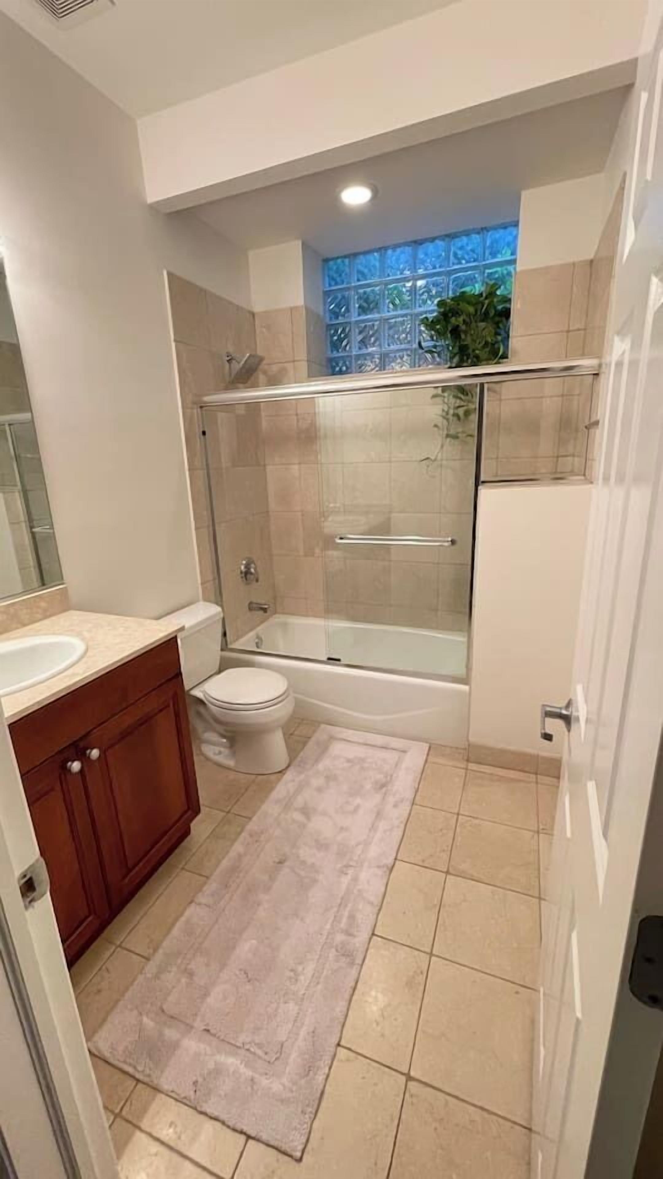 A bathroom with a glass-enclosed shower, a bathtub, a toilet, and a sink with a wooden vanity.