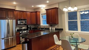 A modern kitchen with stainless steel appliances, wooden cabinets, and a glass dining table. - Ukrainian Village 3BR/3BA • Private Patio, Parking (Chicago)