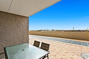 Relax on the patio with a table and two chairs, surrounded by a low wall and a shaded canopy.