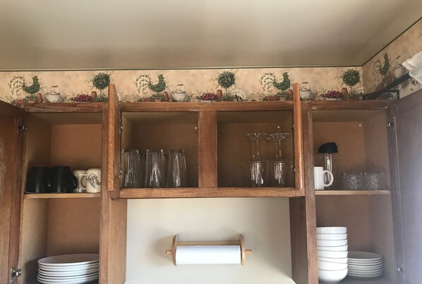 A kitchen with wooden cabinets, shelves with glassware, and a rolling pin on the counter. - Covered parking/3 bedrooms, sitting room, restroom w/laundry, full kitchen, deck (Lead)