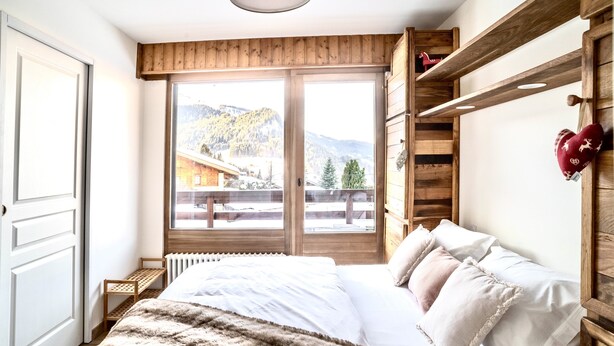 A bedroom with a large bed, wooden headboard, and a view of a mountain landscape through a sliding door. - Fantastic fully renovated flat in Megève (Megève)