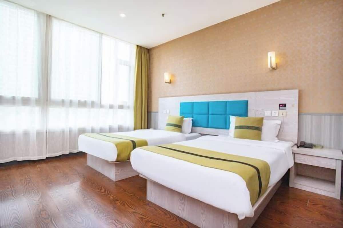 Ein Hotelzimmer mit zwei Betten, einem großen Fenster mit transparenten Vorhängen, Holzboden und einer hellen Wand mit Struktur.