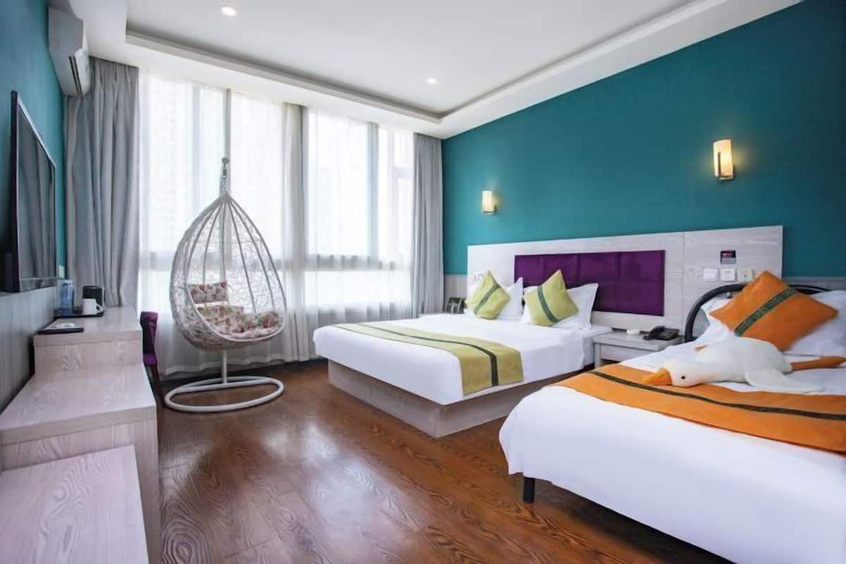 Ein Hotelzimmer mit zwei Betten, einem Hängesessel, einem Schreibtisch und einem Fernseher.