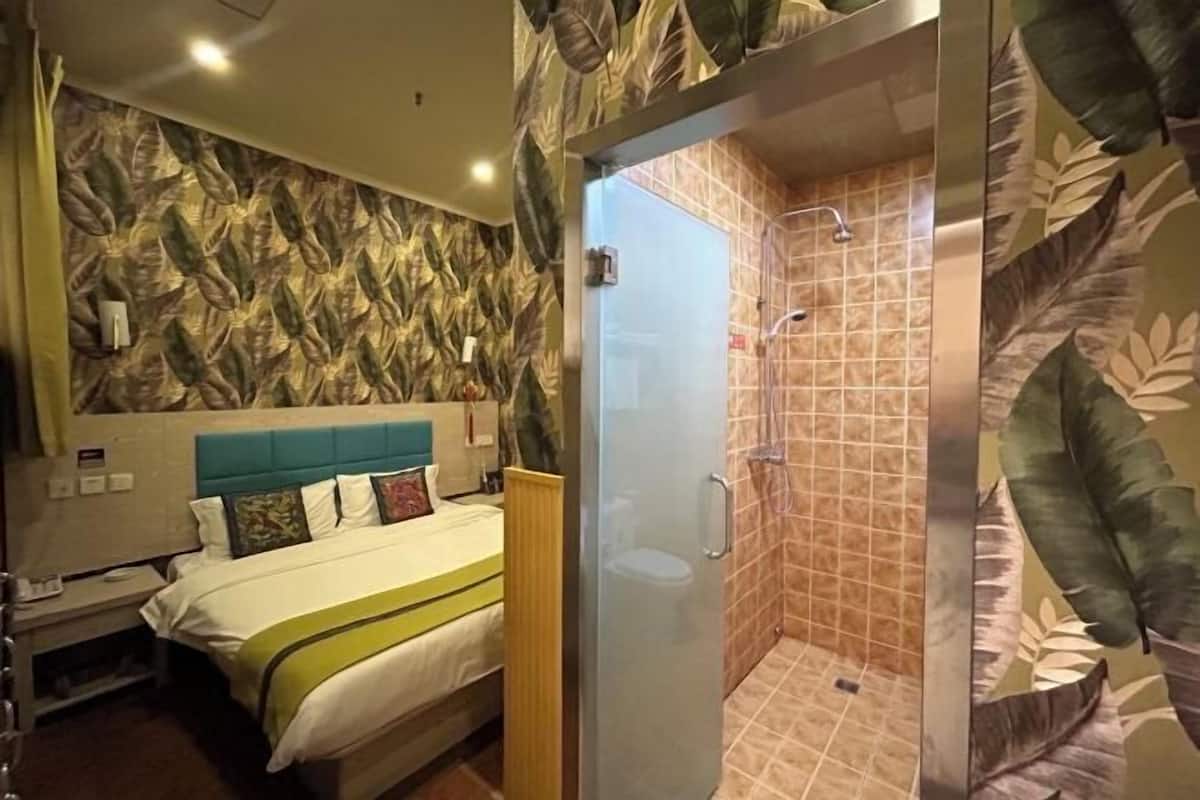Ein Hotelzimmer mit einem Bett, einer Duschkabine und einer Wand mit einem Blattmuster.