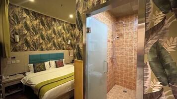 A hotel room with a bed, a shower area, and a wall with a leaf pattern.
