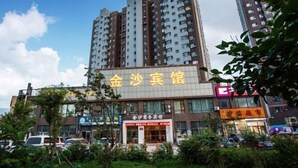 A hotel with a prominent sign in yellow characters, surrounded by other buildings and parked cars. - Changchun Jinsha Hotel (Changchun)