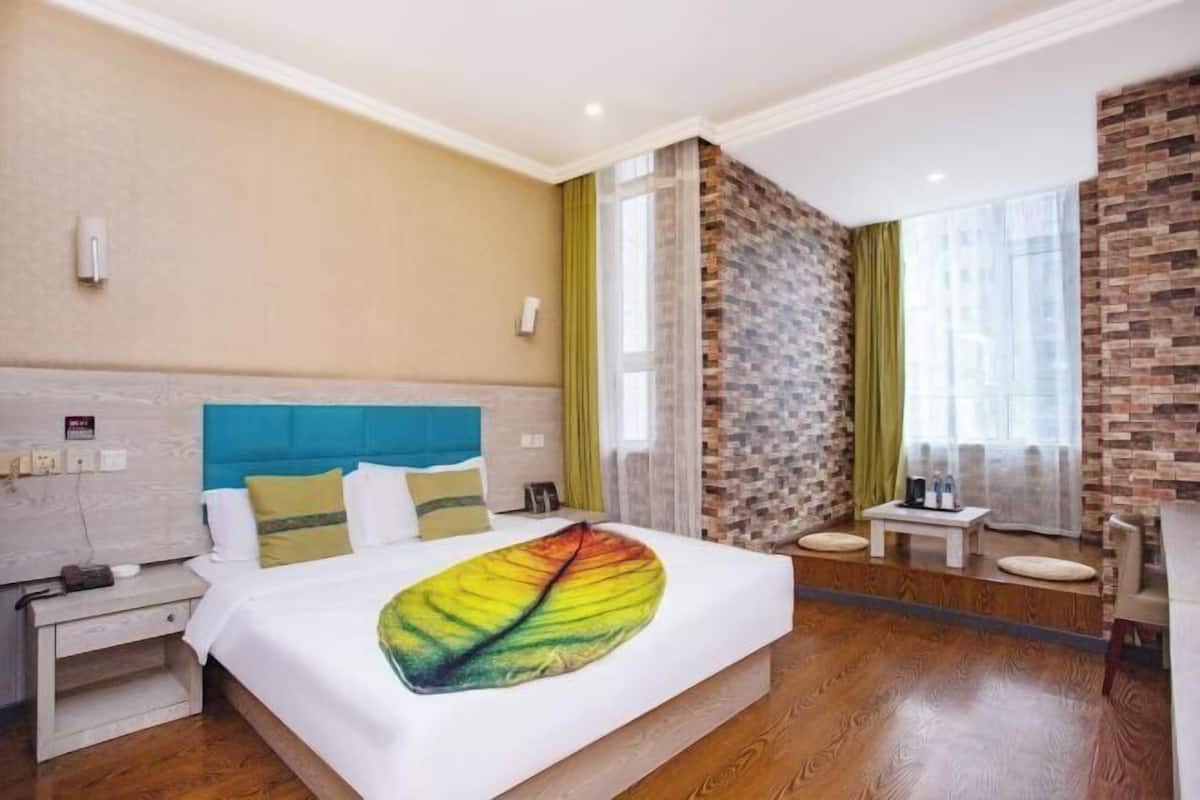 Ein Hotelzimmer mit Bett, Nachttisch, kleinem Tisch und einem Fenster mit Vorhängen.