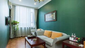 A living room with a sofa, two wooden tables, a potted plant, and a framed picture on the wall.