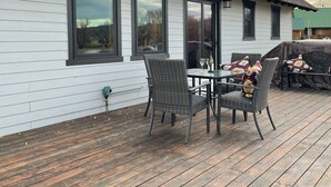 Une maison dotée d’une terrasse, de grandes fenêtres et d’un espace extérieur aménagé et abrité.