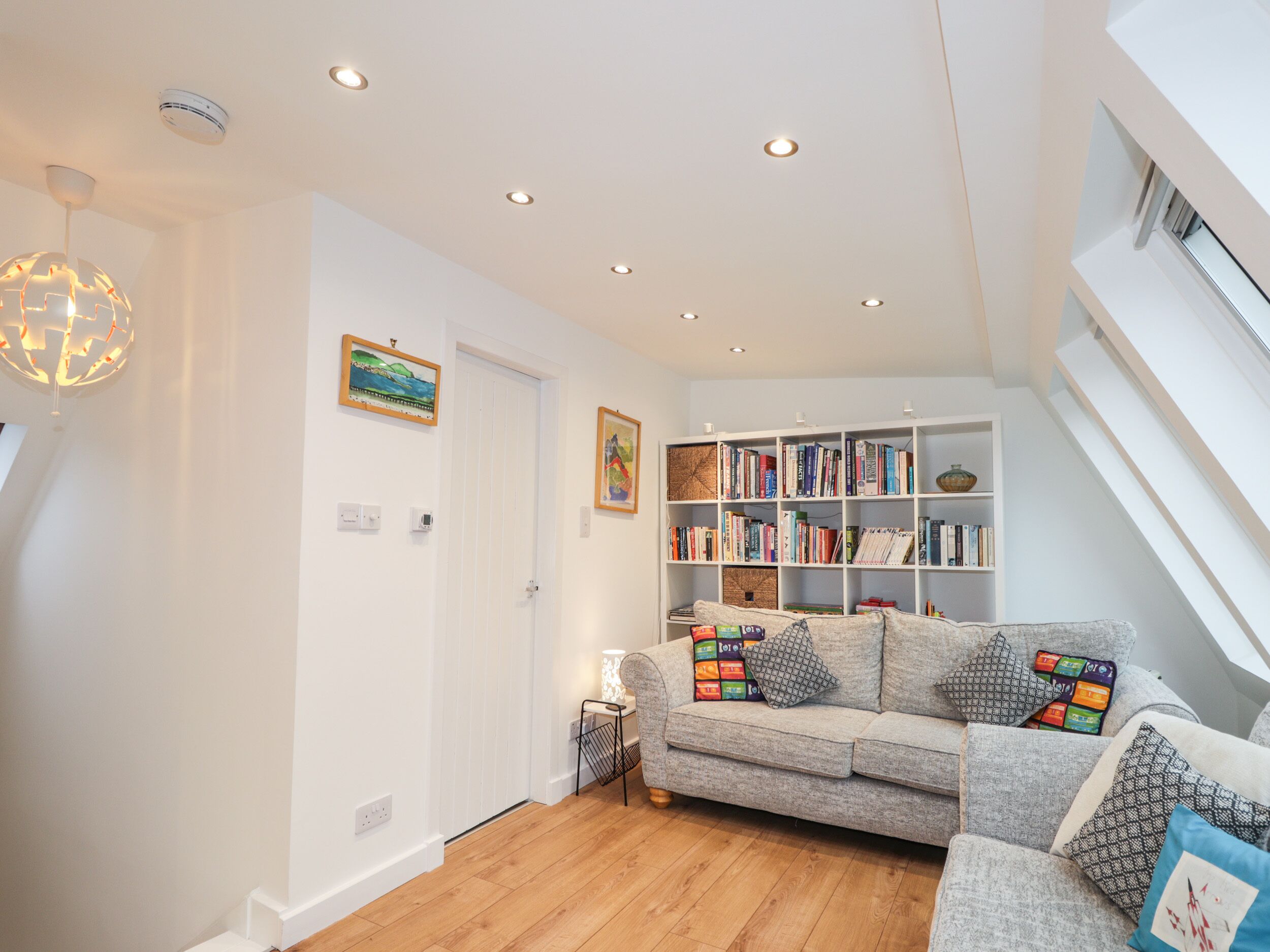 A modern living room with a grey sofa, a bookshelf, and a decorative light fixture.