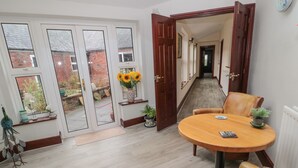 A dining area with a round wooden table, two leather chairs, and a vase of sunflowers on a shelf. - Barnacre (Morpeth)