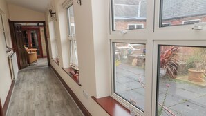A hallway with wooden flooring, a door at the end, and windows overlooking a garden. - Barnacre (Morpeth)