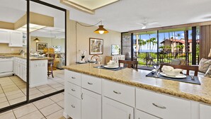 Una cocina moderna con gabinetes blancos, encimeras de granito y vistas a un paisaje tropical a través de amplios ventanales.