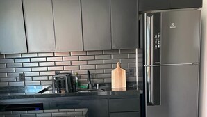 Una cocina moderna con armarios oscuros, un refrigerador de acero inoxidable y una tabla de cortar de madera sobre la encimera.