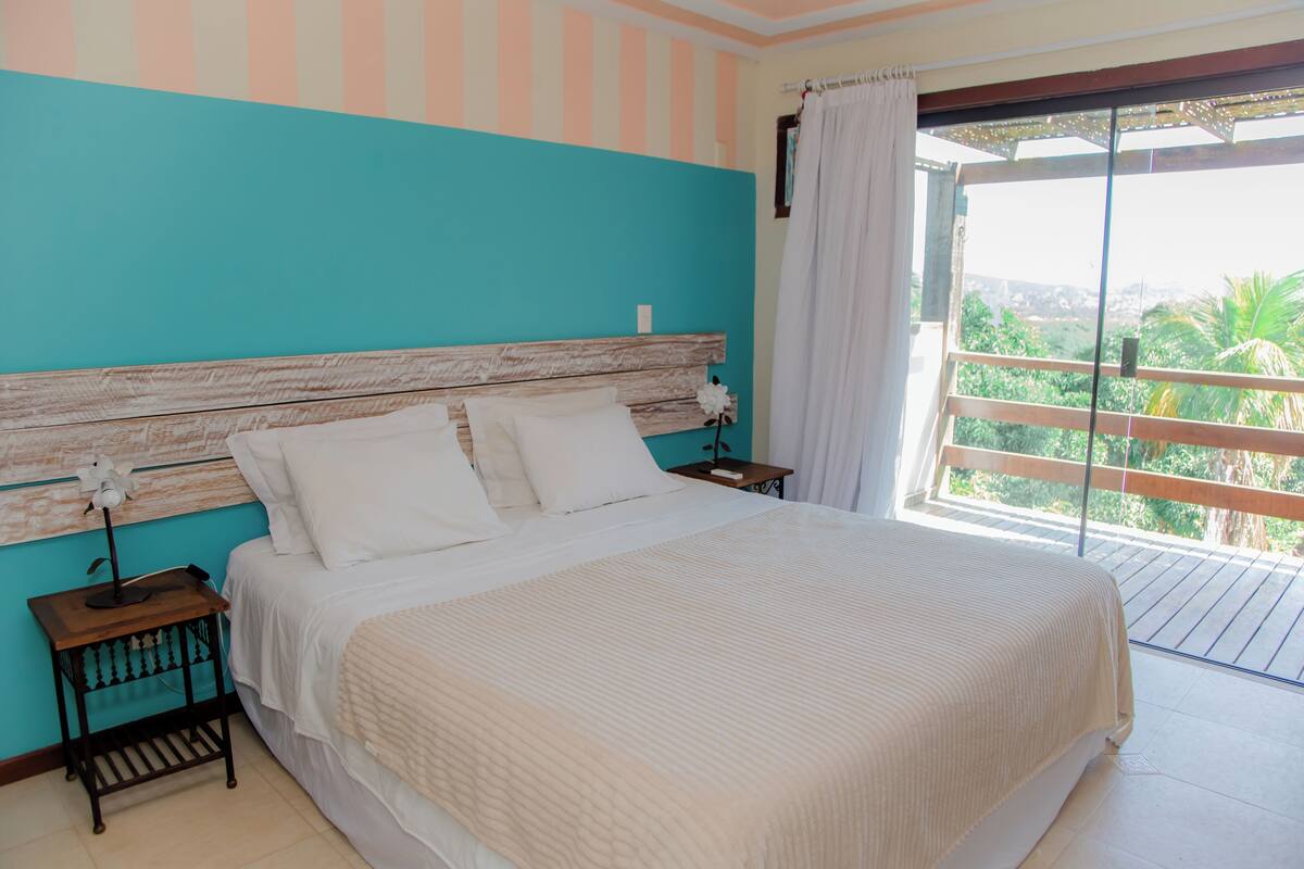 A bedroom with a large bed, a wooden headboard, a nightstand, and a view of the outdoors through a sliding door.