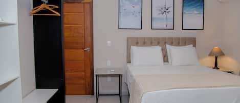 A bedroom with a bed, a bedside table, a nightstand, a hanging coat rack, and three framed pictures on the wall.