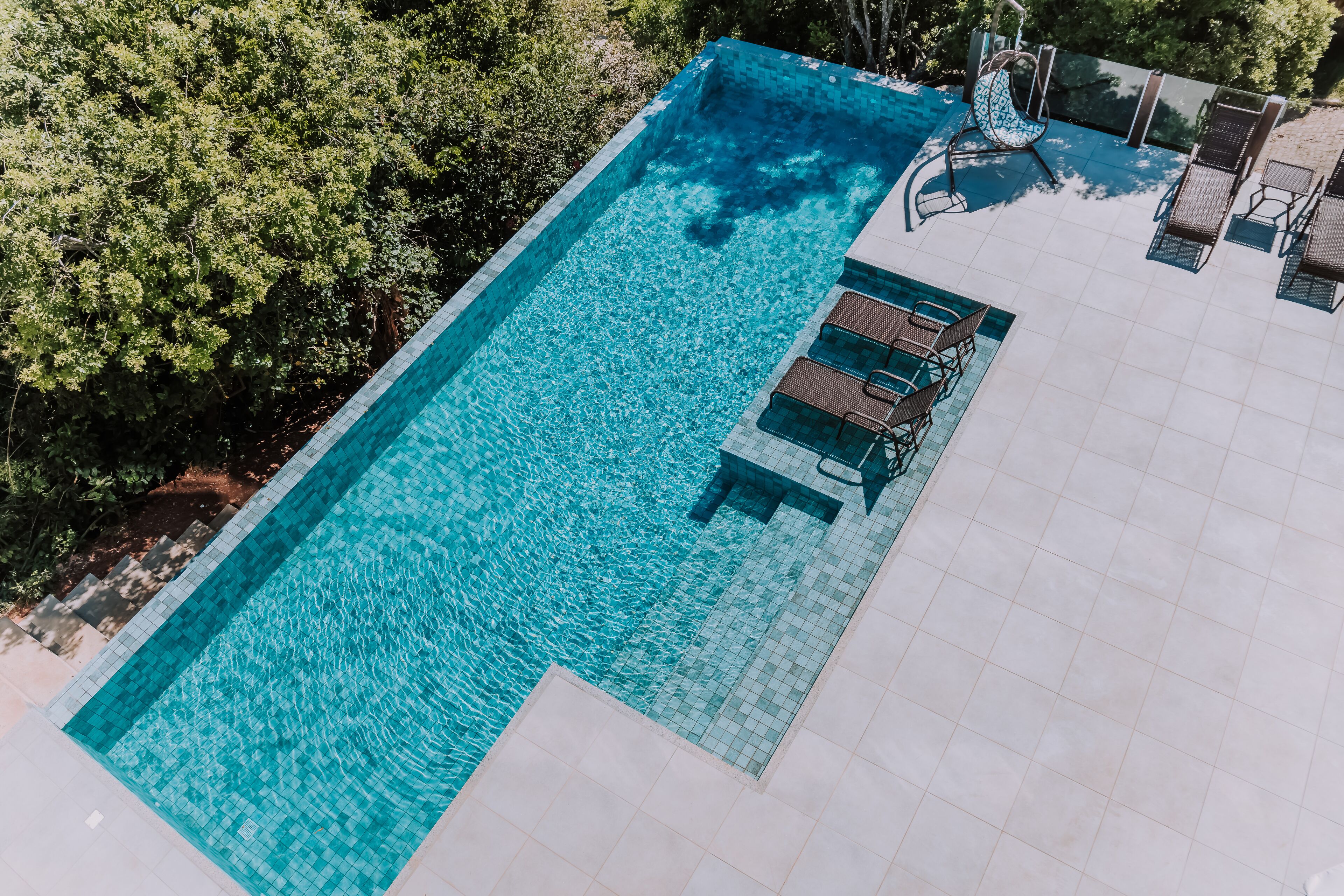A rectangular swimming pool with clear blue water, surrounded by a tiled deck.