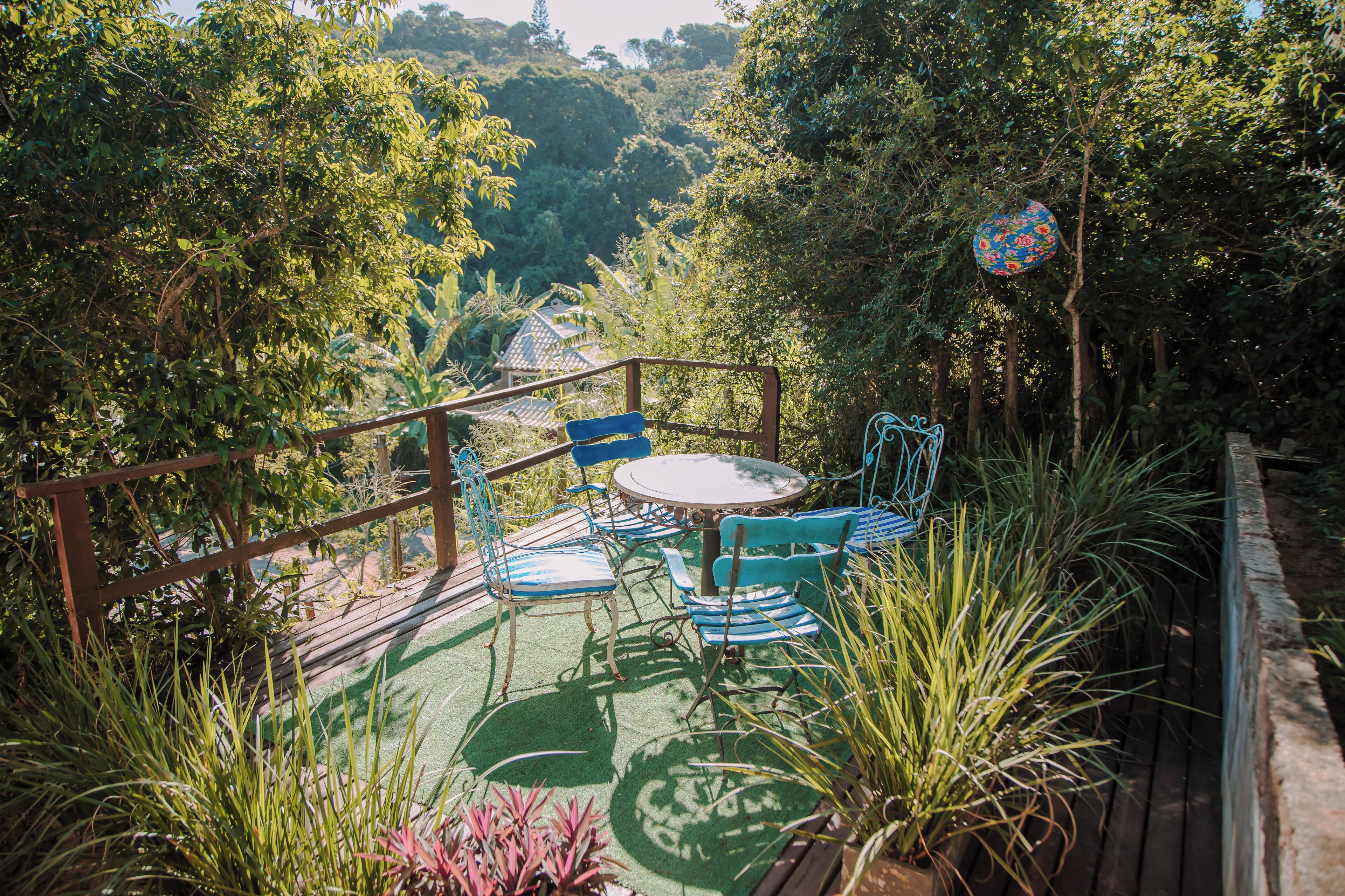 A patio with a round table and chairs, surrounded by lush greenery and a wooden deck.