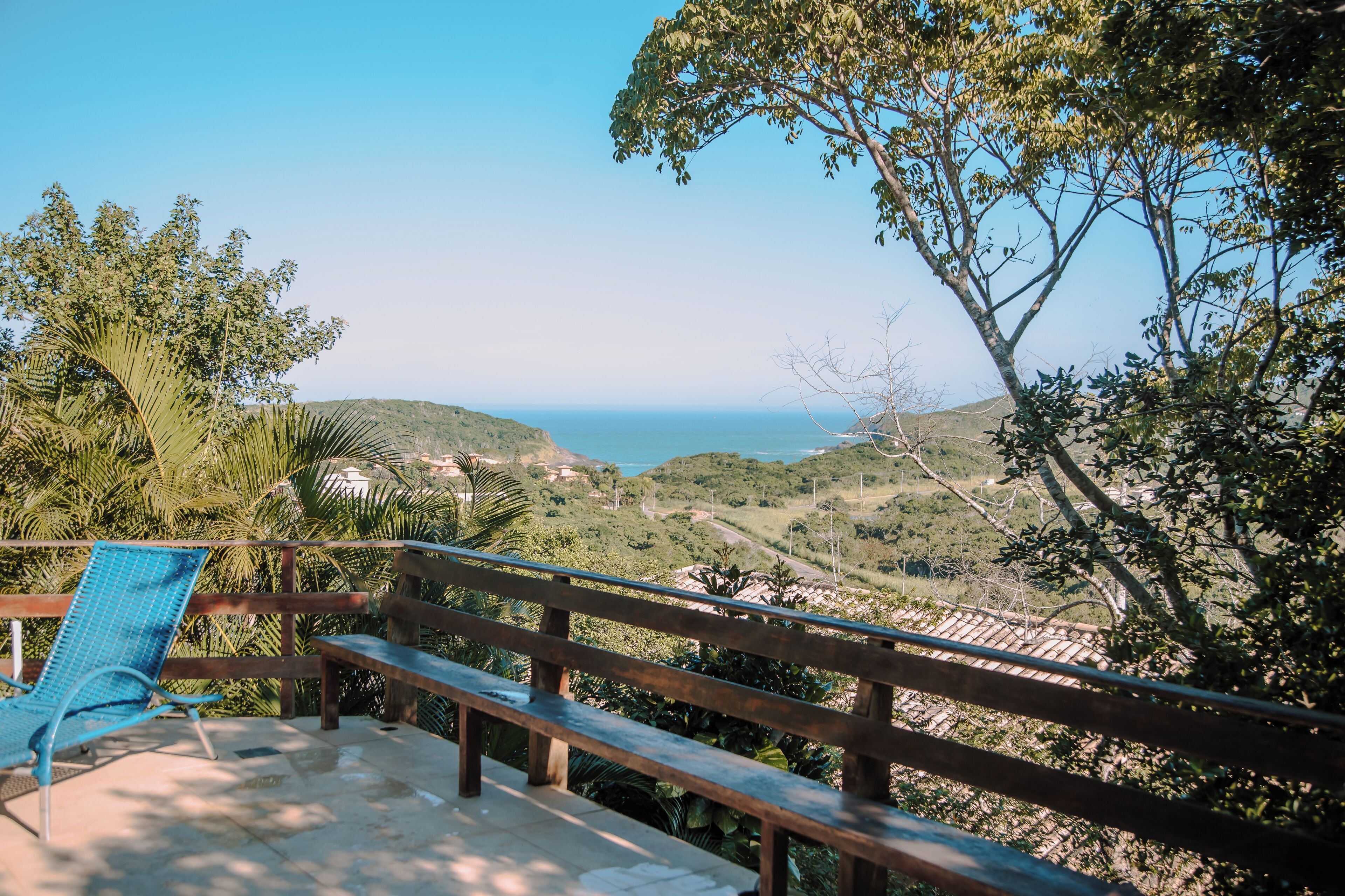 A terrace with a wooden railing, a blue chair, and a view of a coastal landscape.