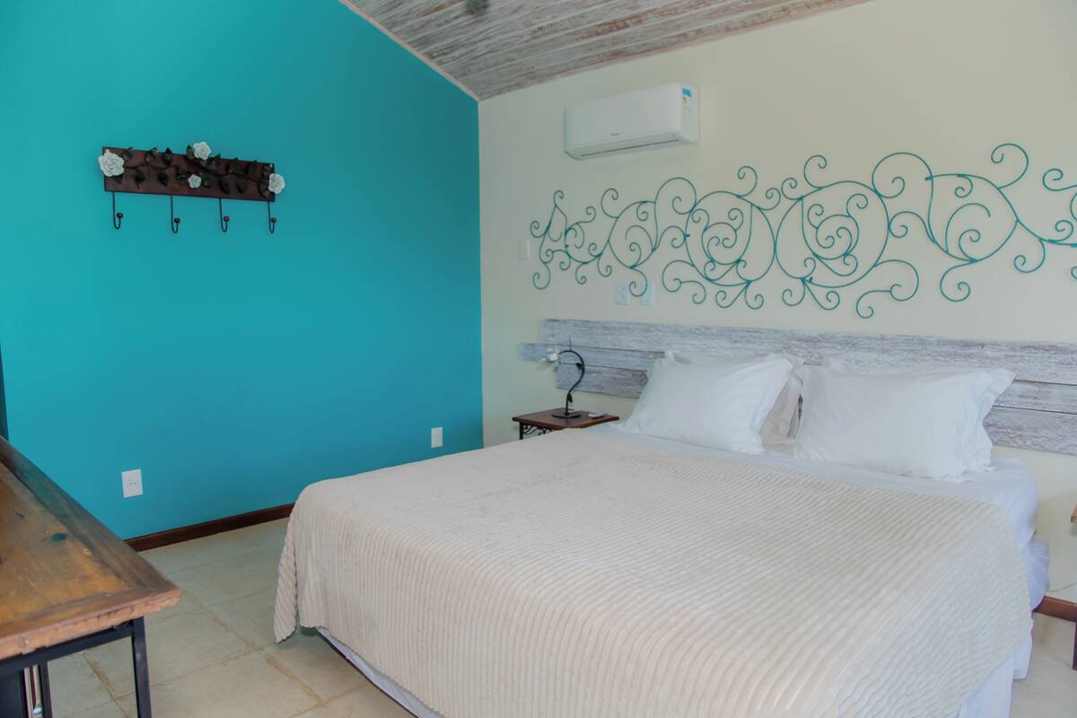 A bedroom with a bed, a wooden nightstand, a wall-mounted air conditioner, and a decorative metal wall piece.