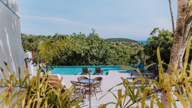 Zona de piscina con sillones reclinables y una mesa, rodeada de follaje y con vistas a una colina.