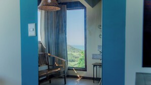 Una habitación con un ventanal grande, un banco de madera, una mesita y una lámpara colgante.