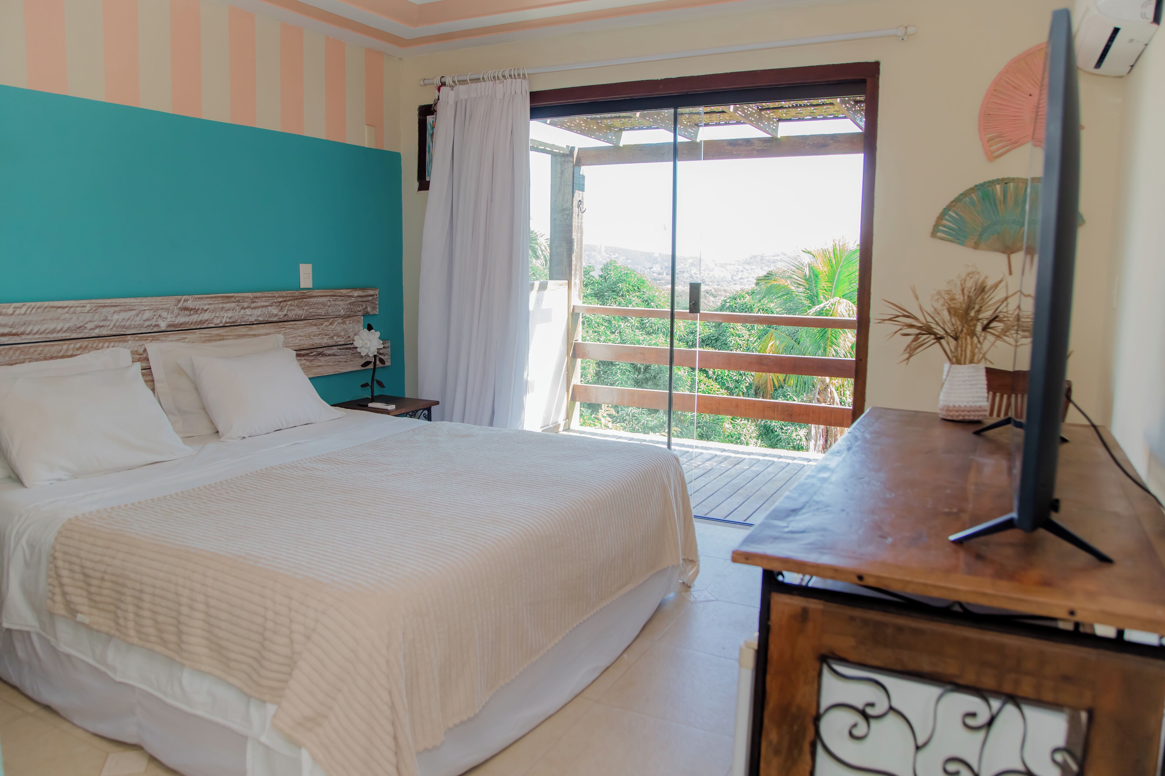 A bedroom with a bed, a nightstand, a TV on a wooden table, and a view of greenery through a sliding door.