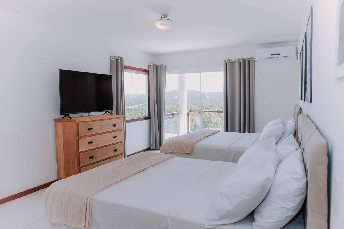 A bedroom with two beds, a TV on a wooden dresser, and a balcony with curtains.